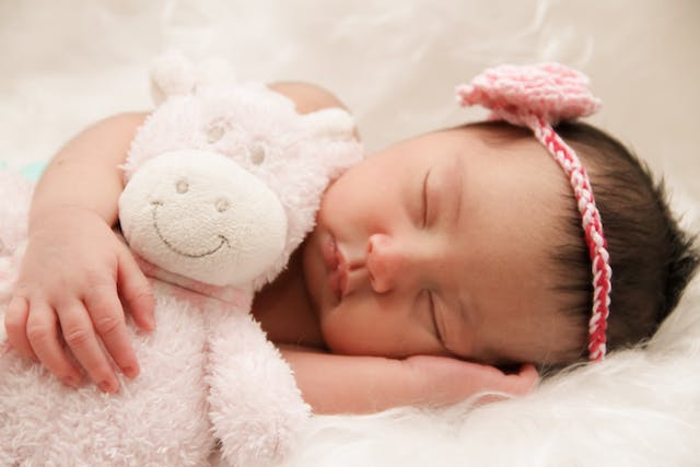 Baby sleeping with a stuffed toy in bed. 